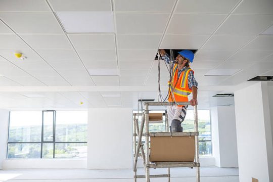 Worker using mobile scaffold tower for ceiling installation indoors