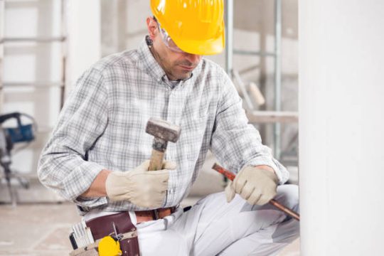 A tradesperson carrying out detailed interior construction work using hand tools, focused on accuracy and finishing within an active building environment.