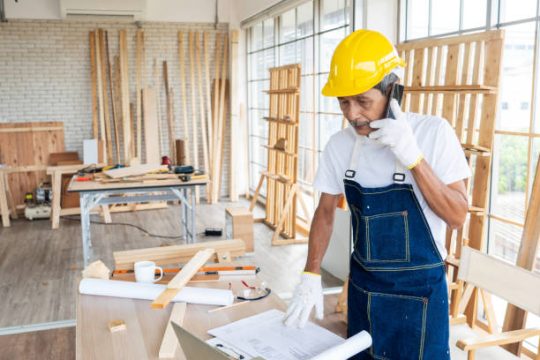 Builder wearing a hard hat reviewing construction drawings in a timber workshop