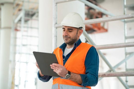 Building site manager inspecting scaffolding area using a digital tablet