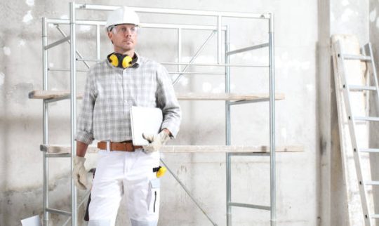 construction supervisor standing on site with scaffolding behind him