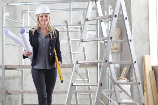 Builder carrying plans near aluminium mobile scaffolds on a construction site