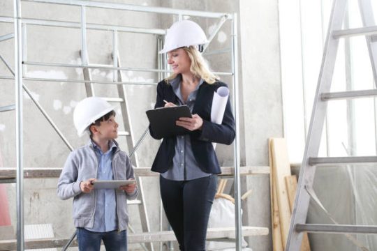 Builder reviewing plans beside scaffold structure while inspecting an indoor construction site