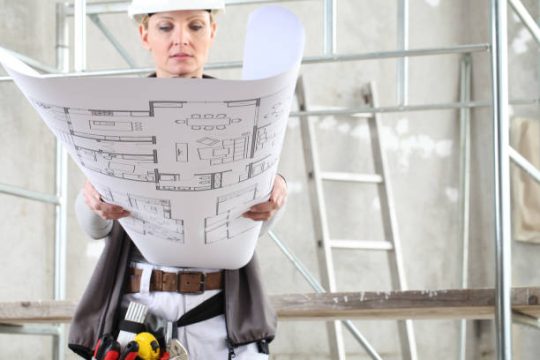 Construction professional reviewing building plans in front of scaffold equipment on an indoor worksite