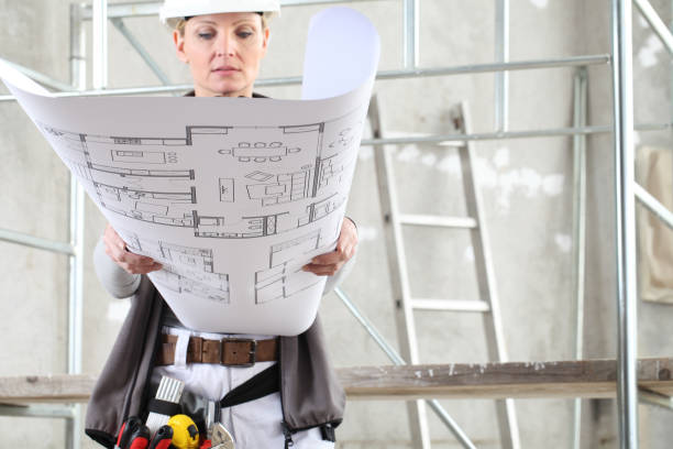 Construction professional reviewing building plans in front of scaffold equipment on an indoor worksite