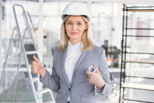 Female construction supervisor reviewing plans on site with scaffolding in the background, showing safe access planning for Kwikstage scaffolding projects.