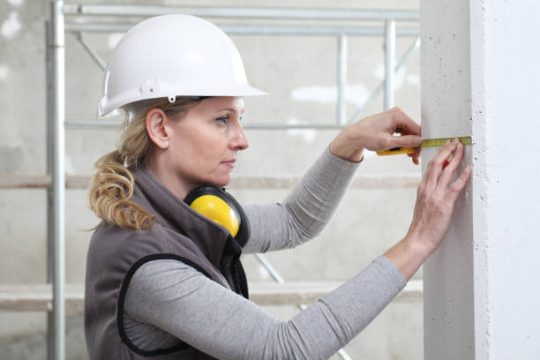 Construction worker measuring wall dimensions beside scaffold equipment