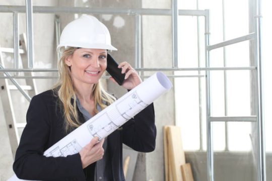 Construction manager holding blueprints beside scaffold structure