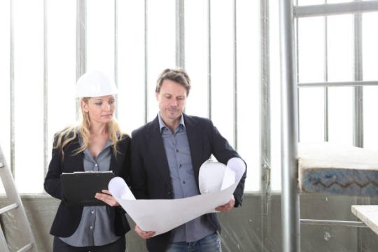 Construction professionals reviewing building plans near scaffolding on an Australian worksite