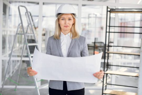 Female construction professional holding building plans beside scaffolding on site