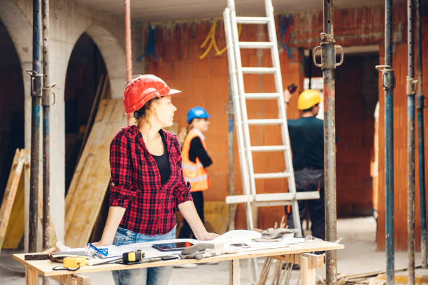 Builder reviewing construction plans on worksite with scaffolding and ladder