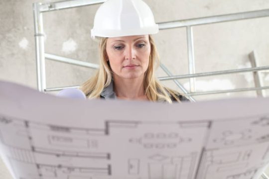 Female construction professional reviewing building plans in front of scaffold structure