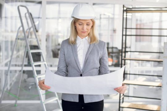 Construction manager checking plans beside scaffold and ladder on site